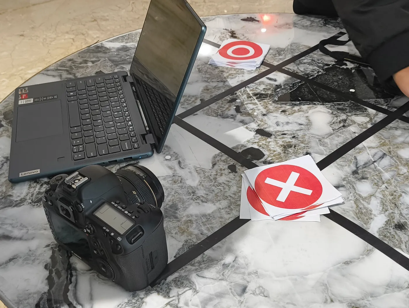 Laptop and DSLR camera on a marble floor next to a red X stage marker