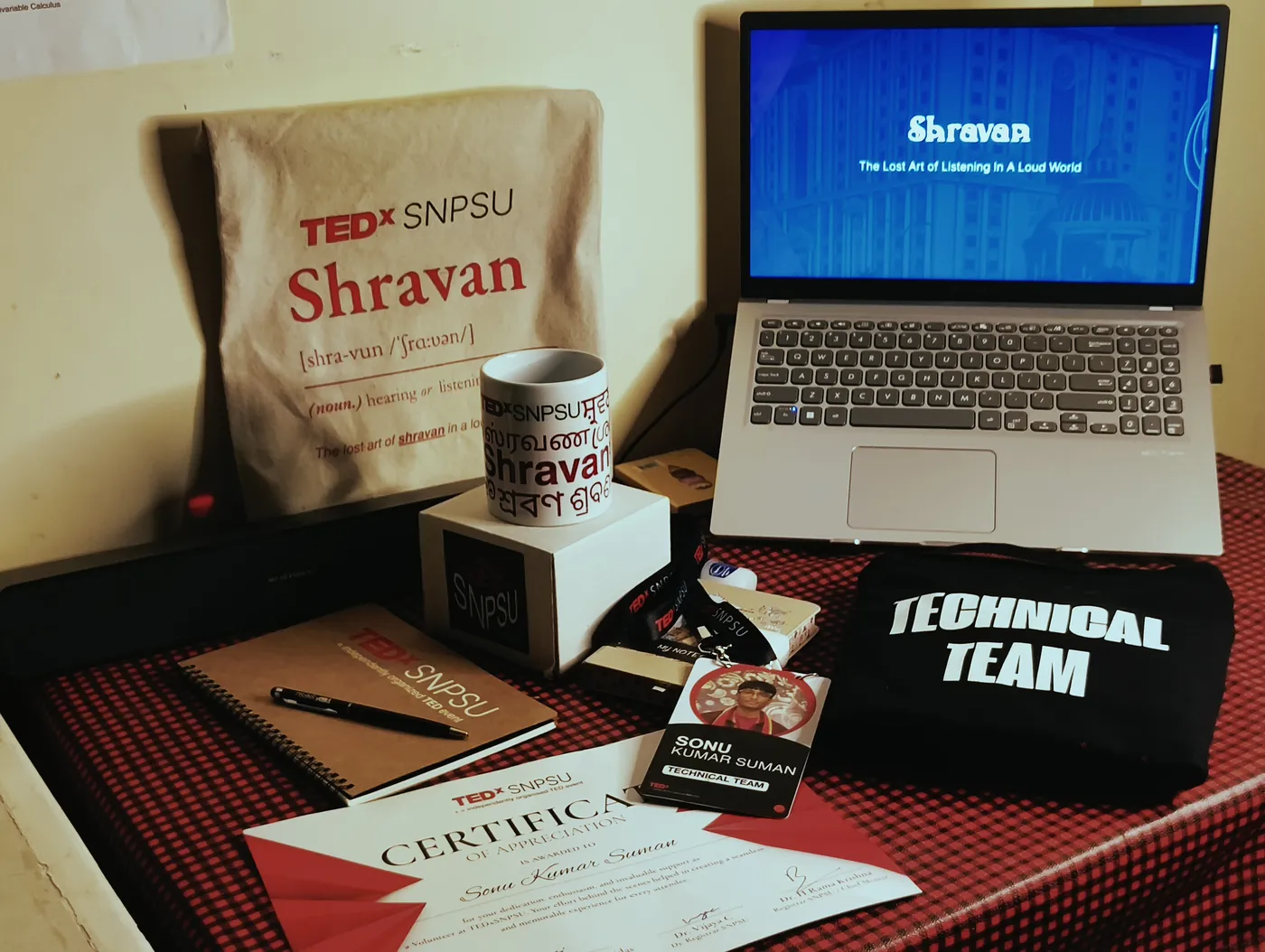 TEDxSNPSU Shravan tote bag, technical team T-shirt, mug and certificate laid out beside a laptop