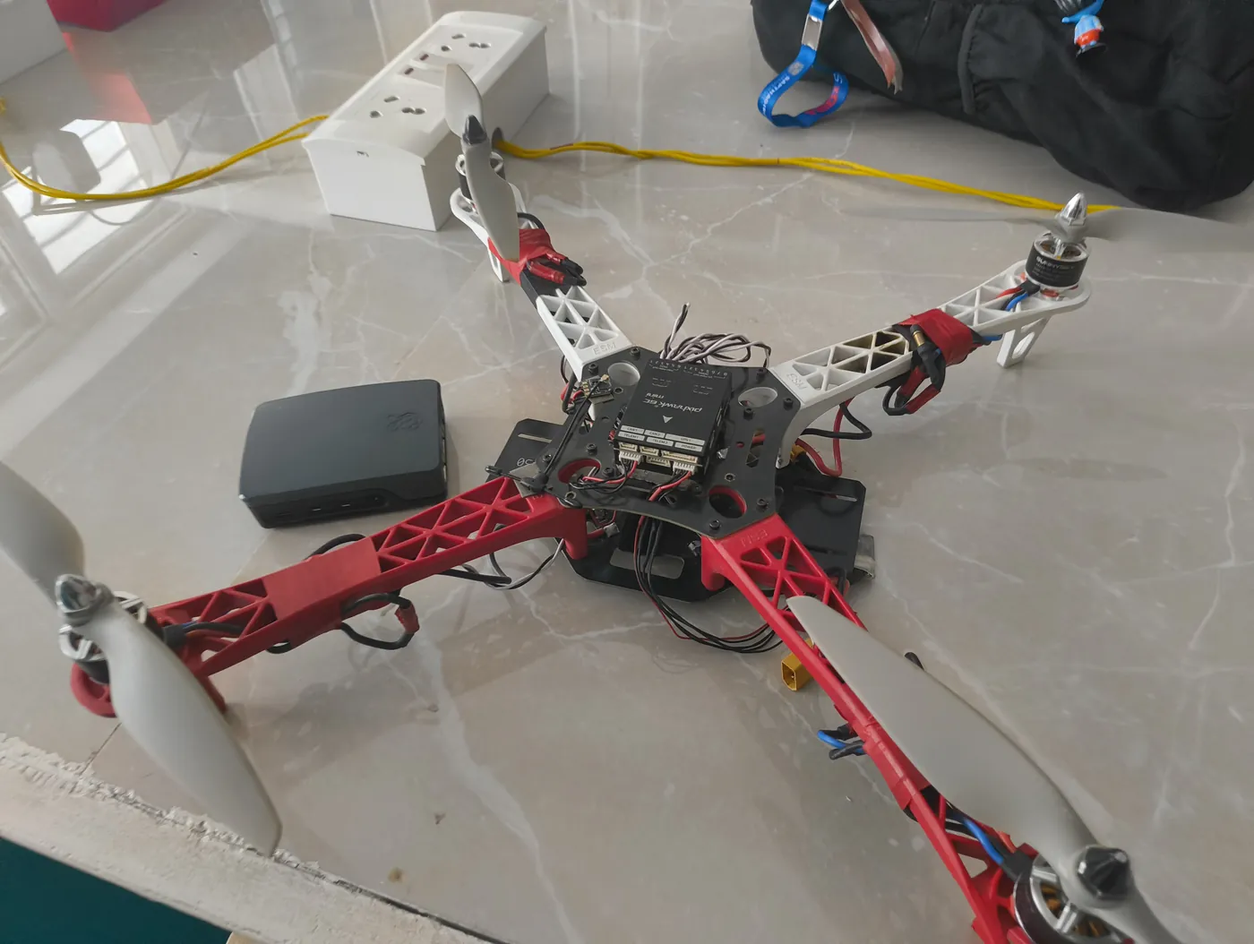 Quadcopter drone frame with red and white arms being assembled on a table