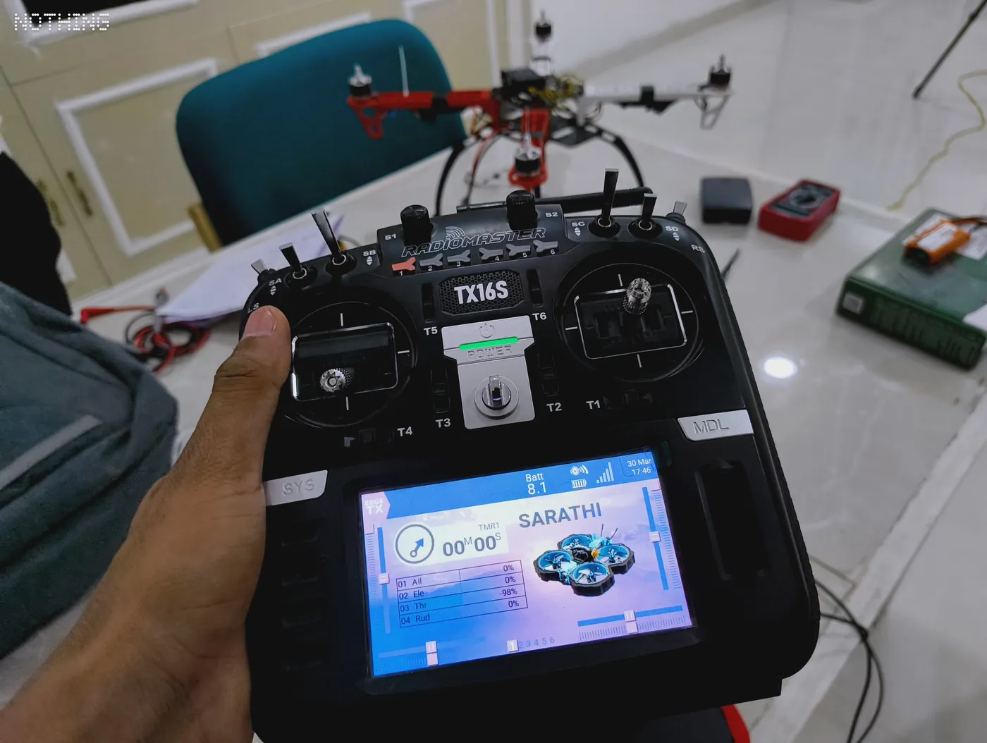 Hand holding a TX16S radio transmitter with its colour screen switched on