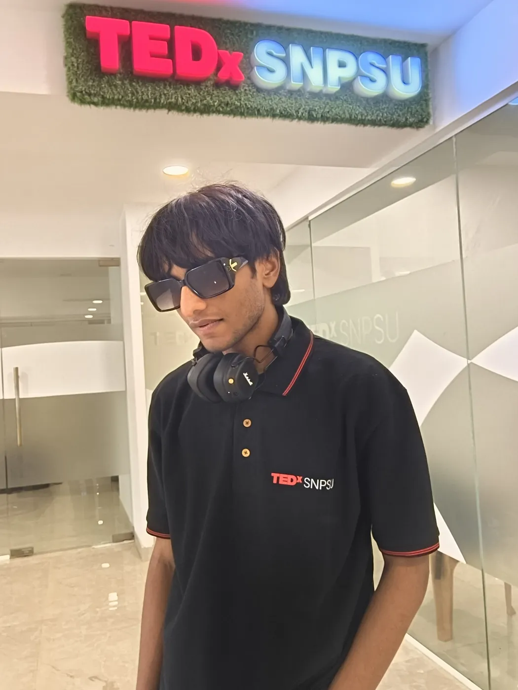 Sonu Kumar Suman standing under the illuminated TEDxSNPSU sign in a TEDx polo shirt