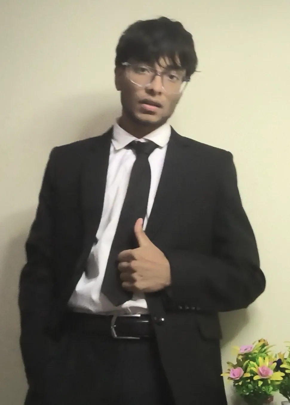 Sonu Kumar Suman in a black suit, white shirt and black tie, giving a thumbs up