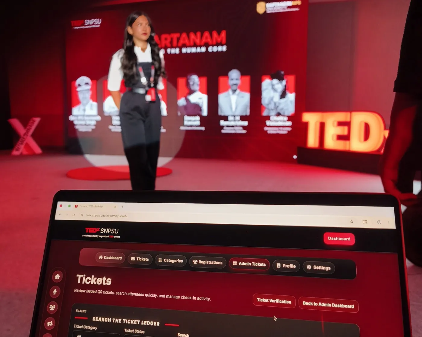 TEDxSNPSU ticketing dashboard open on a laptop with a speaker on stage in the background
