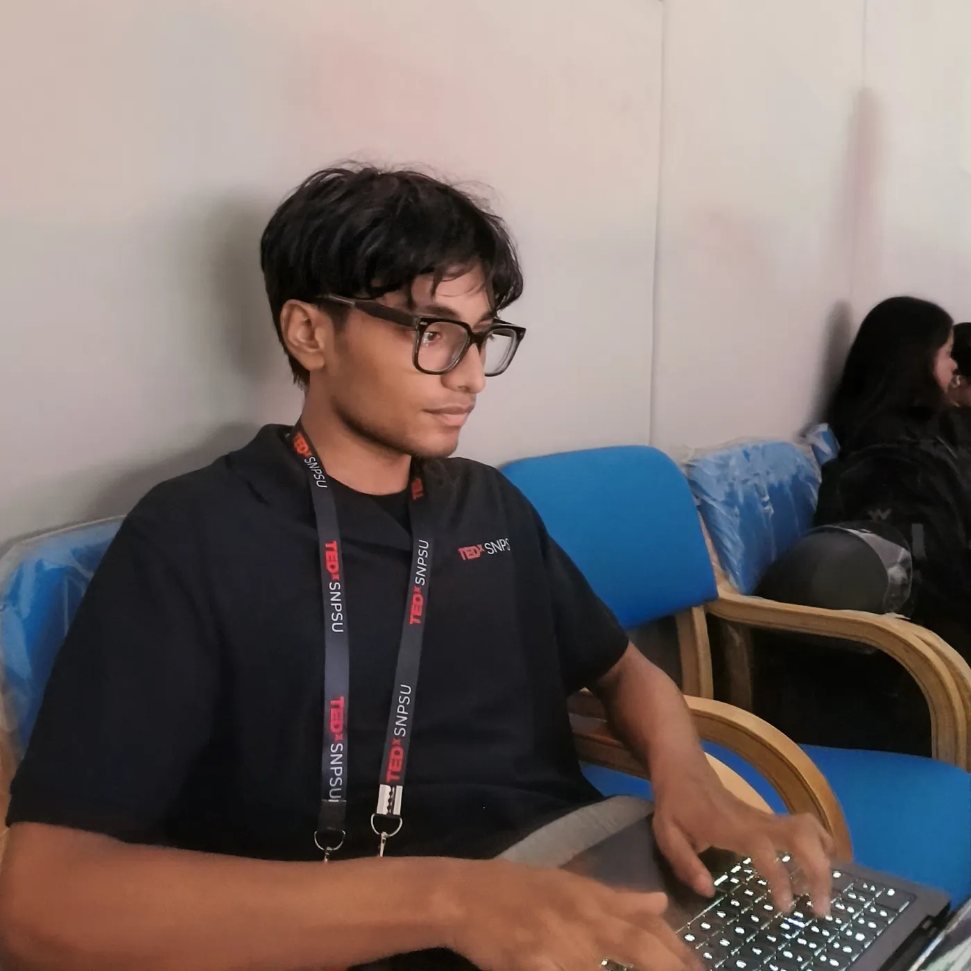 Sonu Kumar Suman in a TEDxSNPSU polo and lanyard typing on a laptop backstage